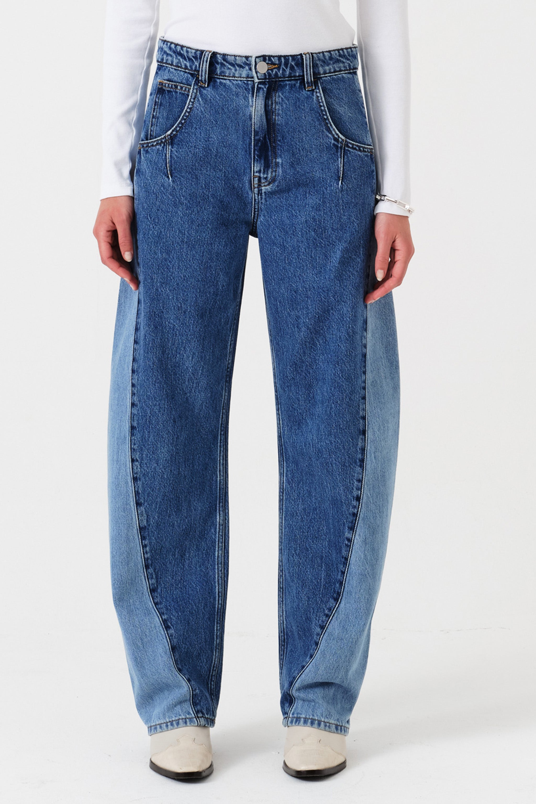 Woman wearing two toned blue barrel leg jeans and a white shirt on a white background