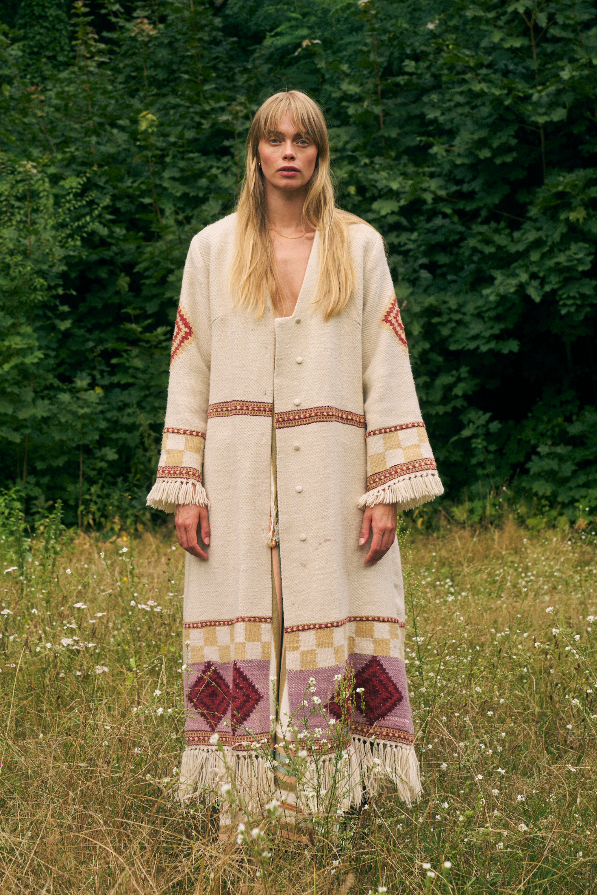 Lady in a field wearing an ankle length vanilla coloured wool coat 